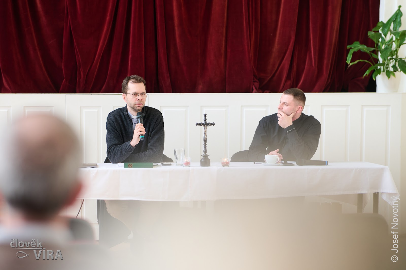 Three speakers at a white table in front of red curtains