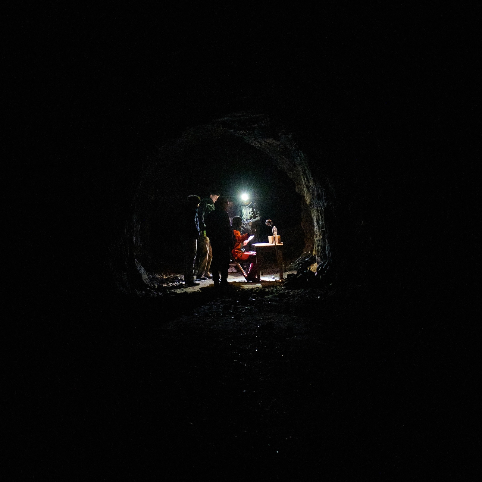 Silhouettes with a torch at the end of a dark tunnel