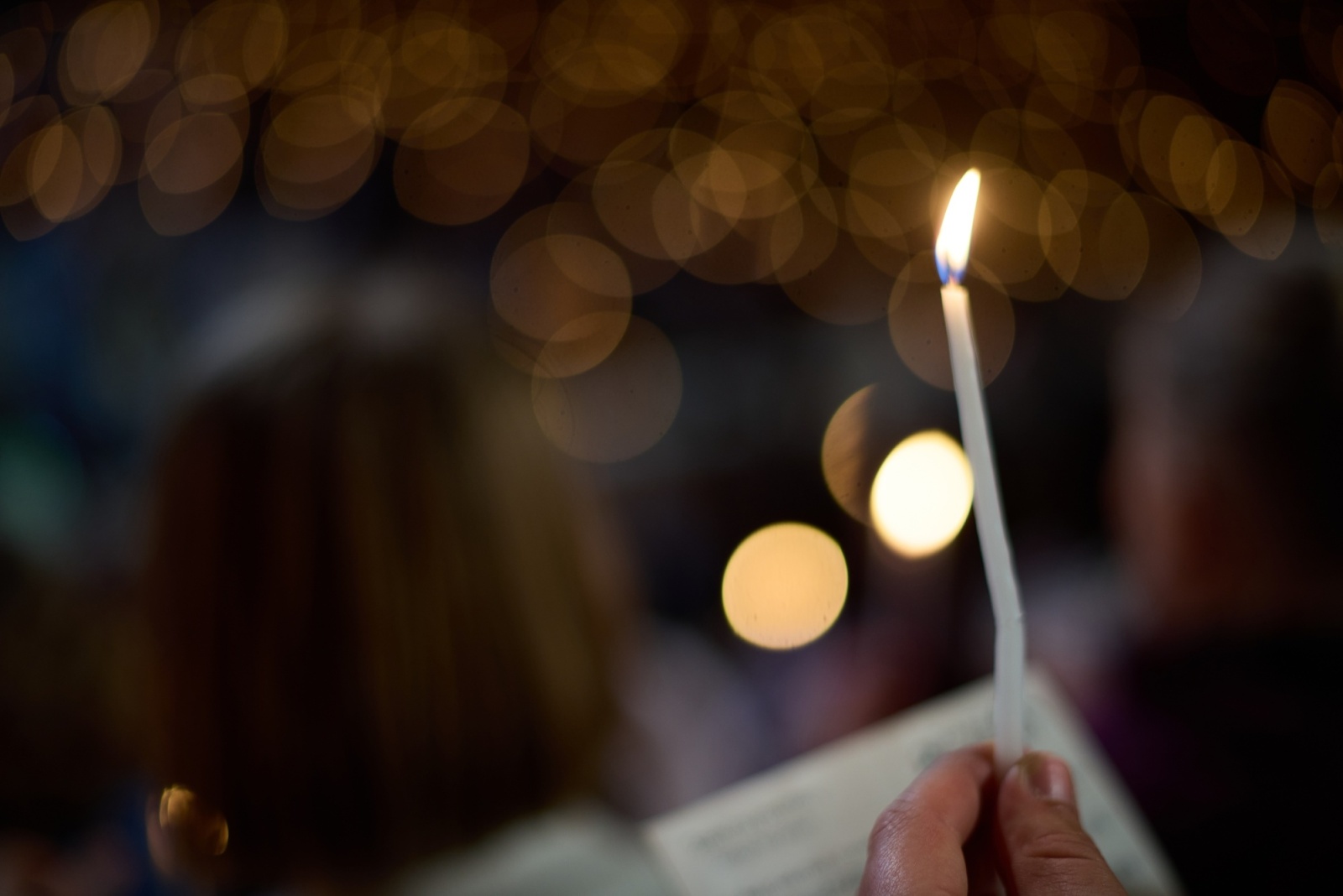 A single candle held up among soft bokeh lights